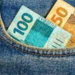 Notas de 100 e 50 reais em bolso de jeans azul